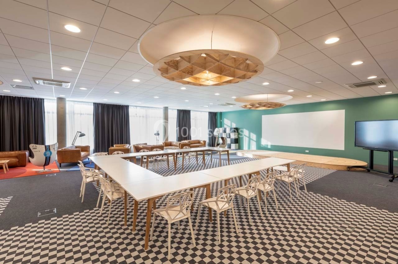 Salle de réunion lumineuse avec tables disposées en U, chaises blanches, tableau blanc et écran interactif.