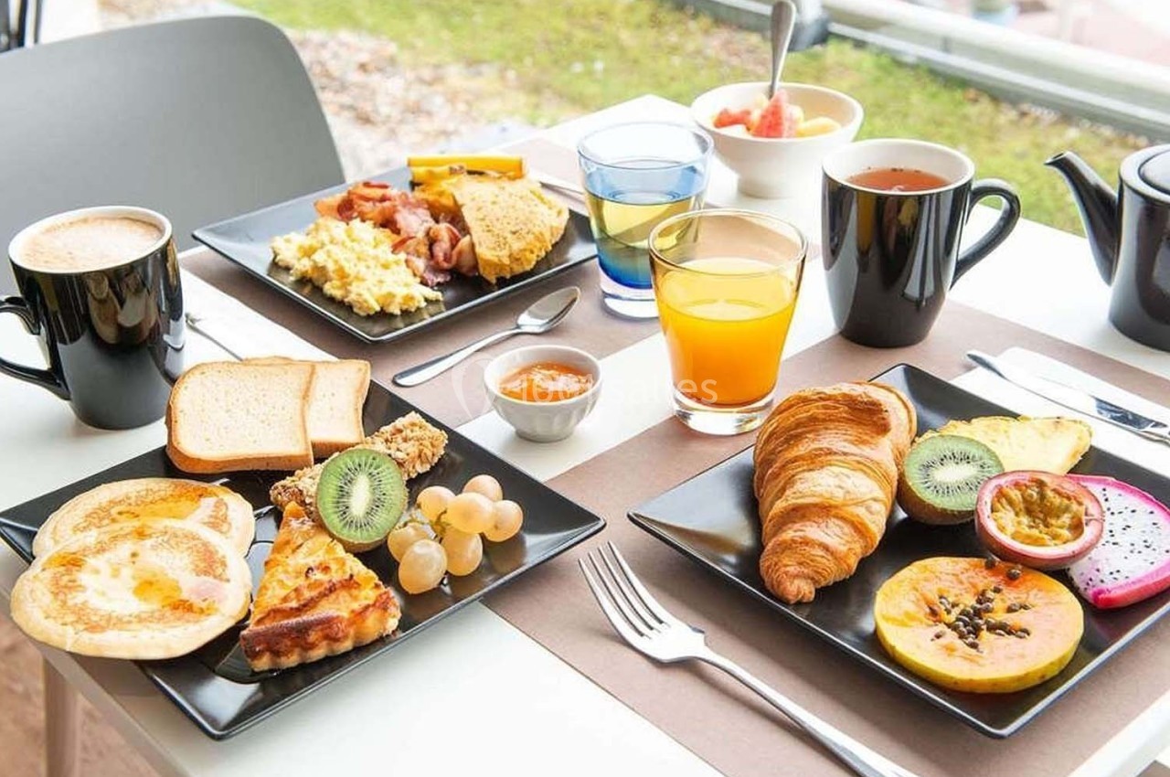 Petit-déjeuner varié avec croissants, fruits, œufs, pain, boissons chaudes et jus sur une table dressée.