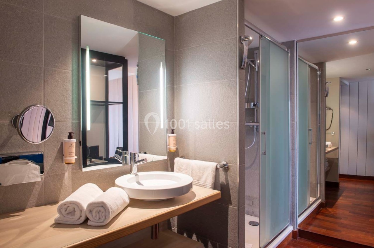 Salle de bain moderne avec lavabo, miroir éclairé, serviettes pliées et douche vitrée en arrière-plan.