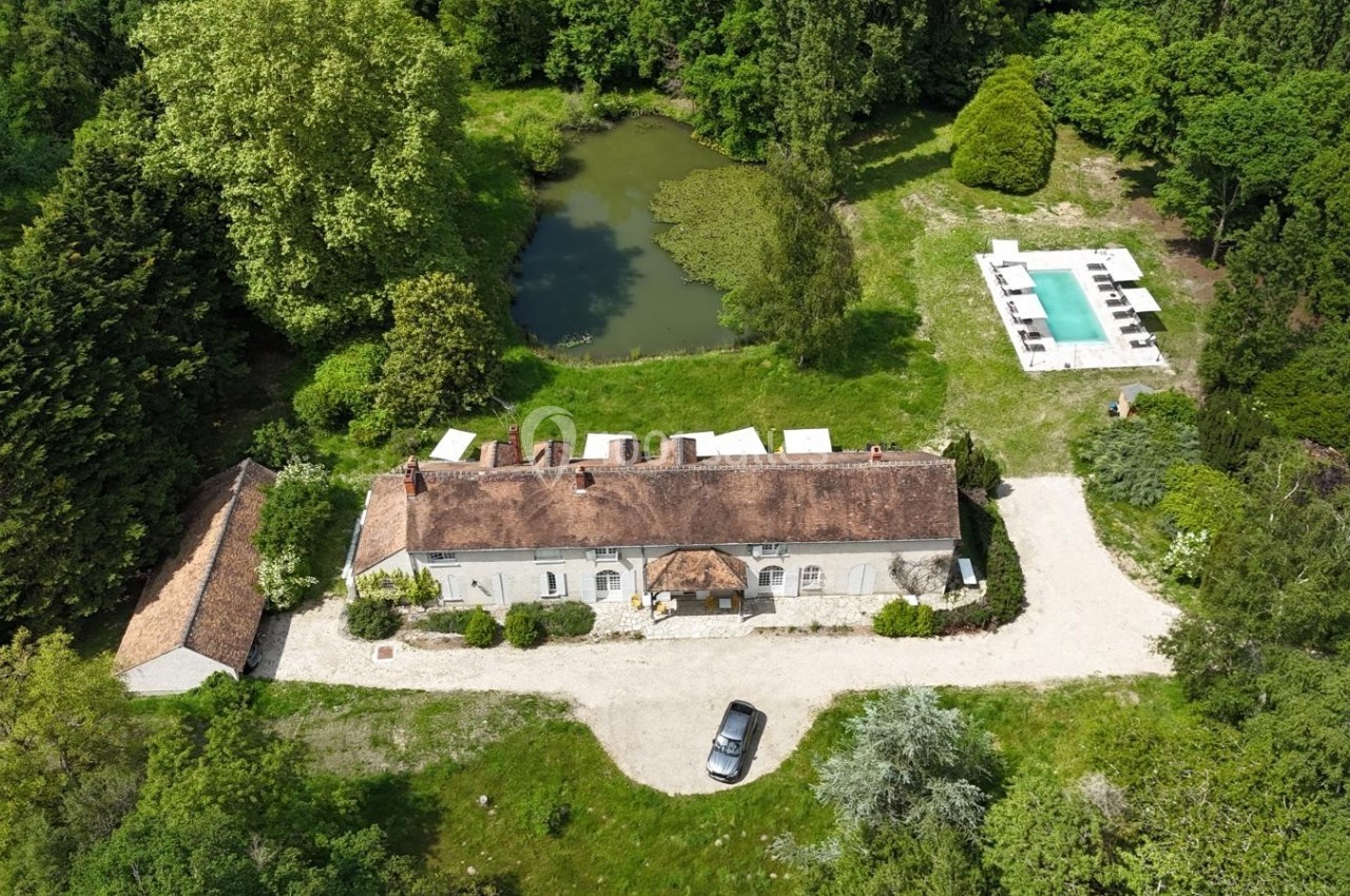 Vue aérienne d'une maison en pierre entourée de verdure, avec un étang et une piscine à proximité.