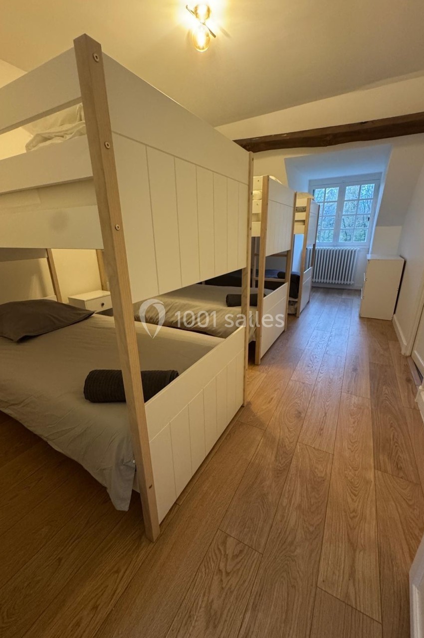 Chambre avec lits superposés en bois, draps gris et lumière naturelle entrant par une fenêtre à carreaux.