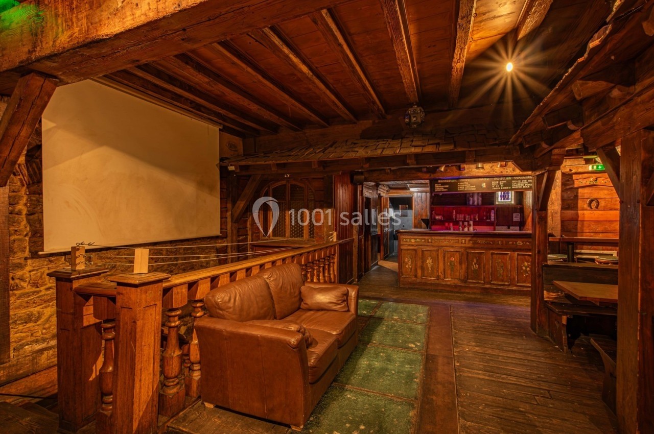 Intérieur d'une pièce rustique avec poutres en bois, canapé en cuir, écran blanc et comptoir en arrière-plan.