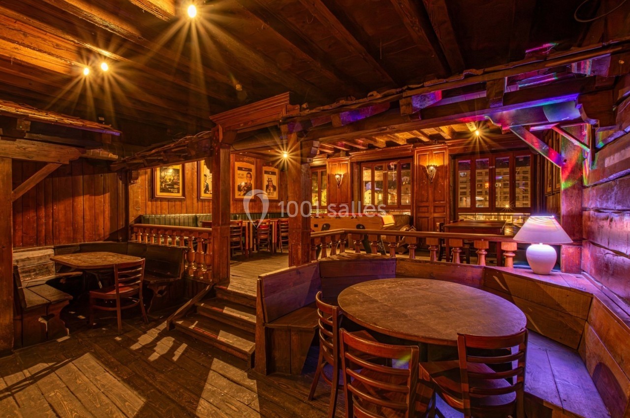 Intérieur d'un restaurant en bois avec tables rondes, chaises, éclairage chaleureux et ambiance rustique.