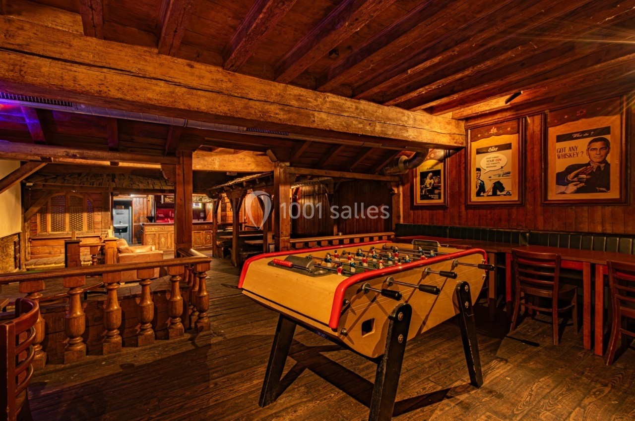 Baby-foot en bois dans un bar rustique avec des murs et un plafond en bois, éclairage chaleureux.