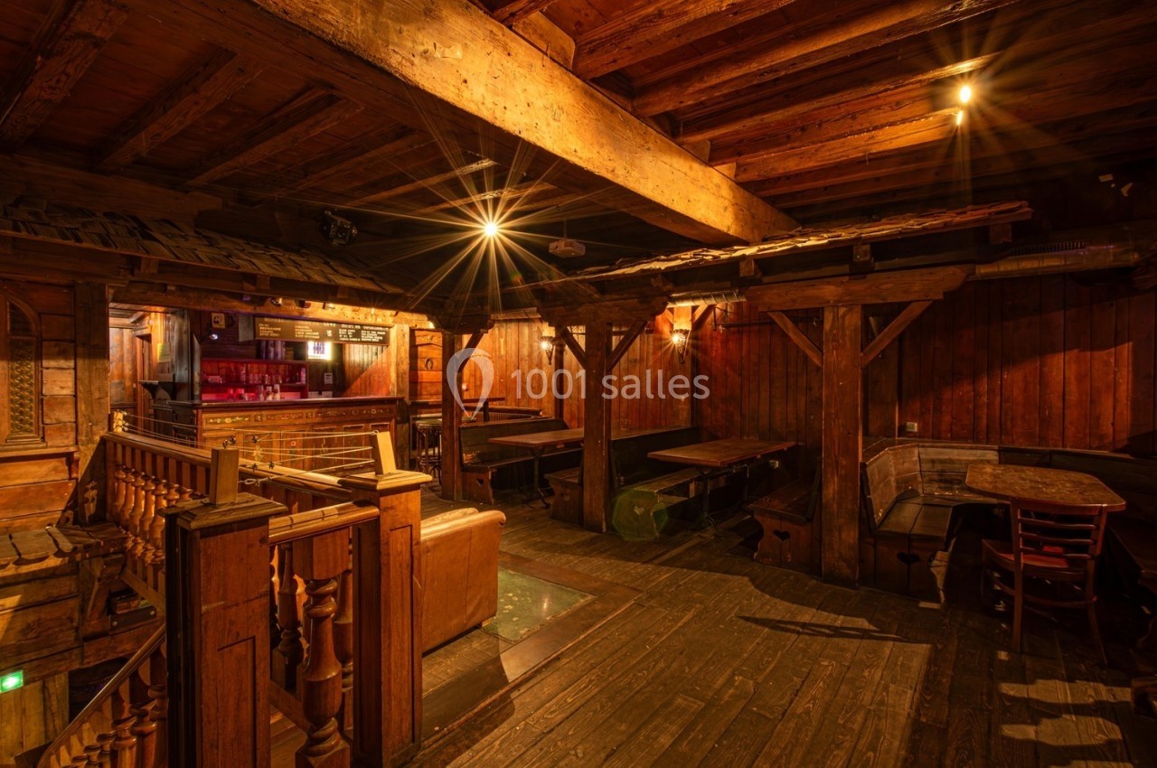 Intérieur d'un bar rustique en bois avec des tables, des bancs et un éclairage chaleureux.