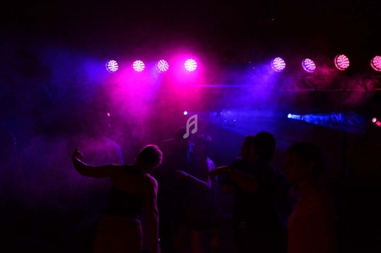 Personnes dansant sous des lumières colorées violettes et bleues dans une ambiance de soirée sombre.
