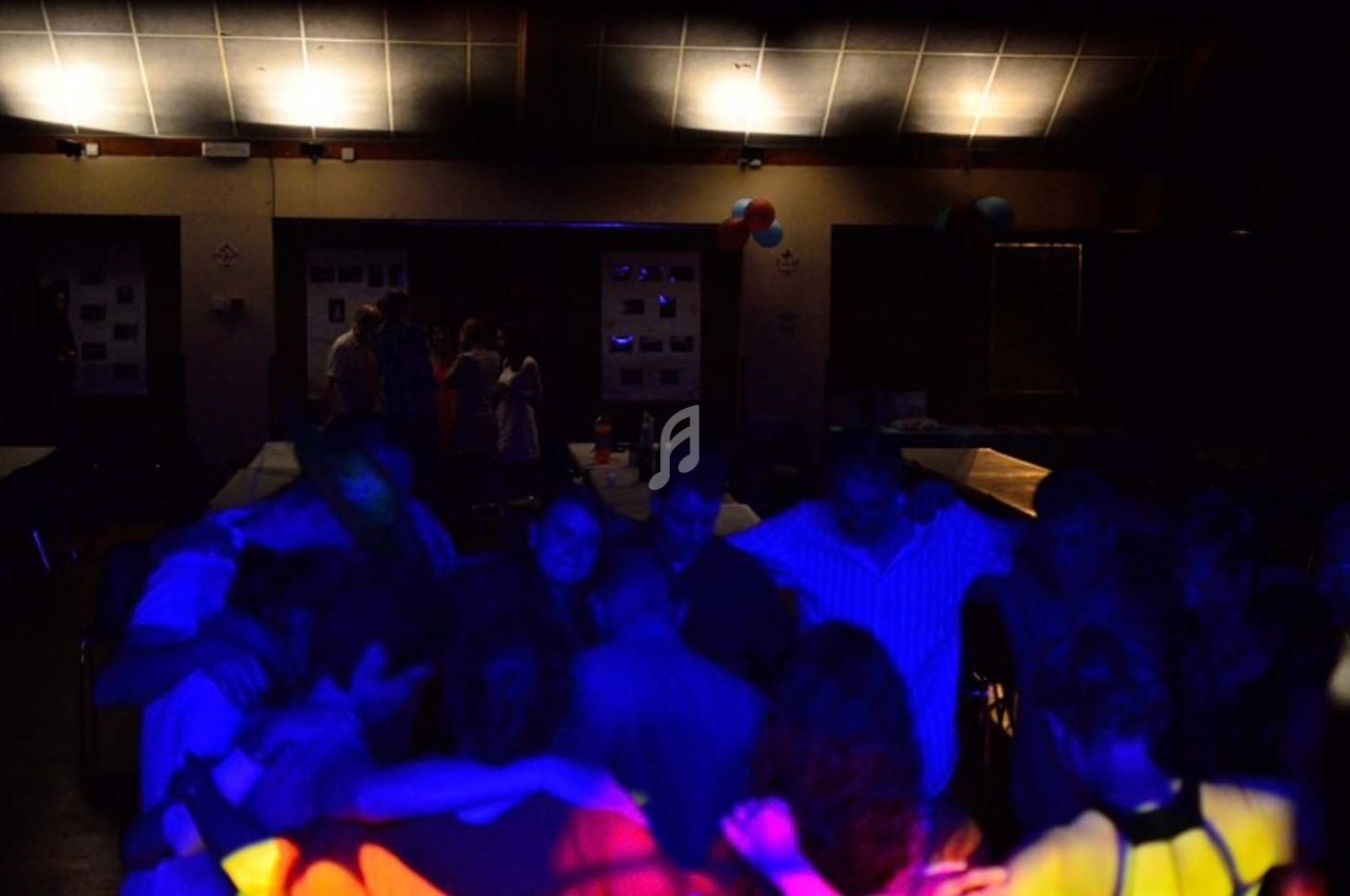 Des personnes dansent dans une salle faiblement éclairée avec des lumières colorées créant une ambiance festive.