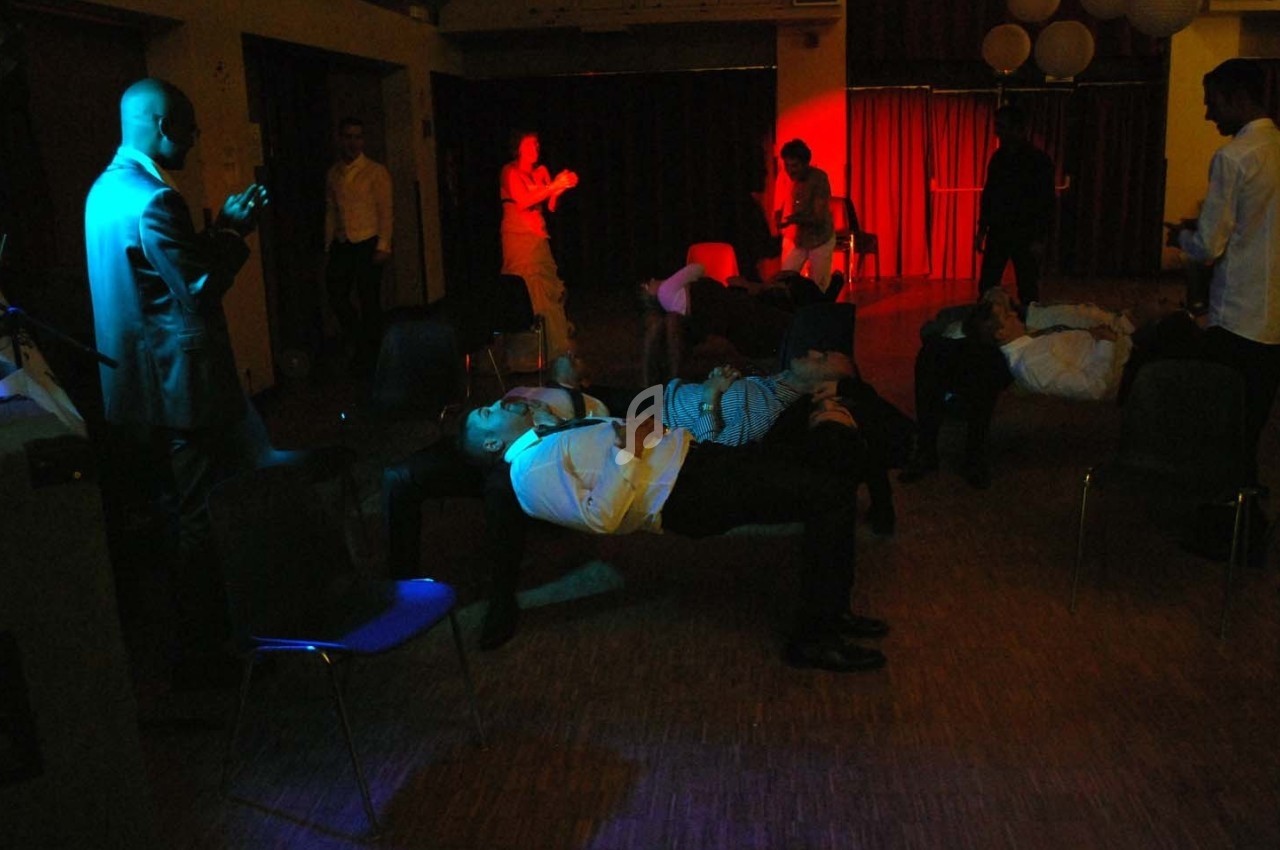 Des personnes allongées sur des chaises dans une salle faiblement éclairée, avec des jeux de lumières colorées.