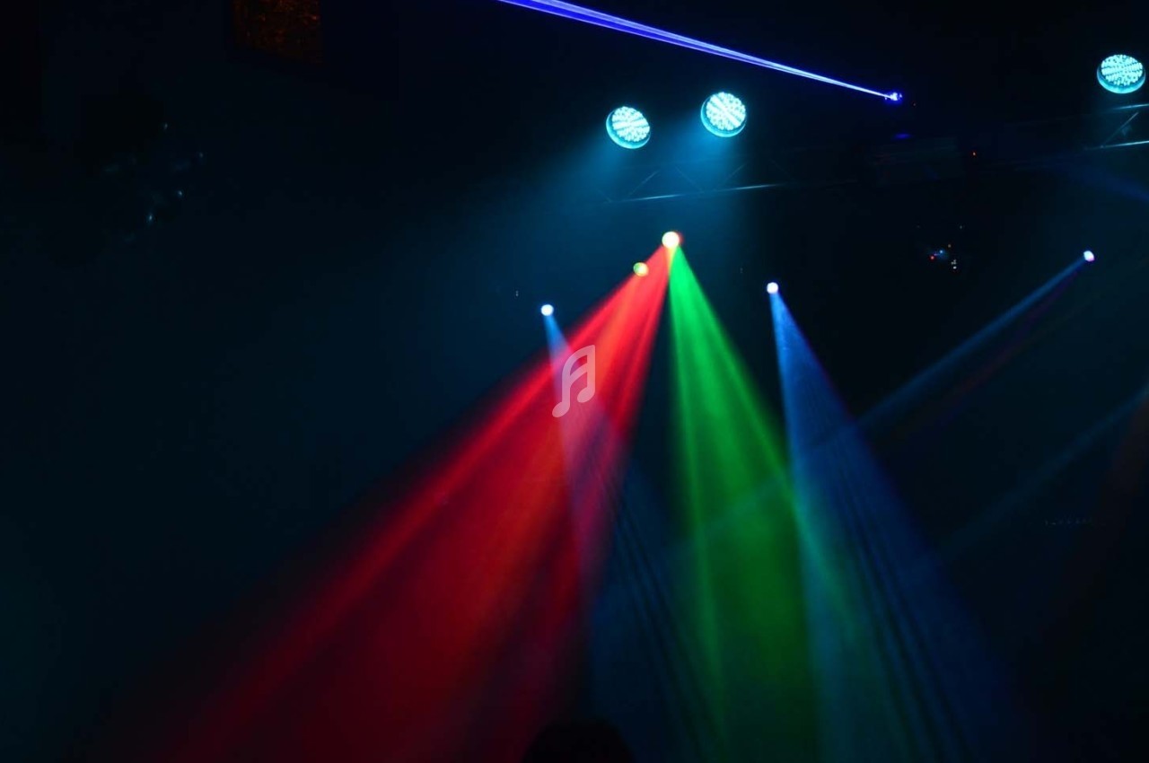 Projecteurs diffusant des faisceaux lumineux rouge, vert et bleu dans une ambiance sombre.
