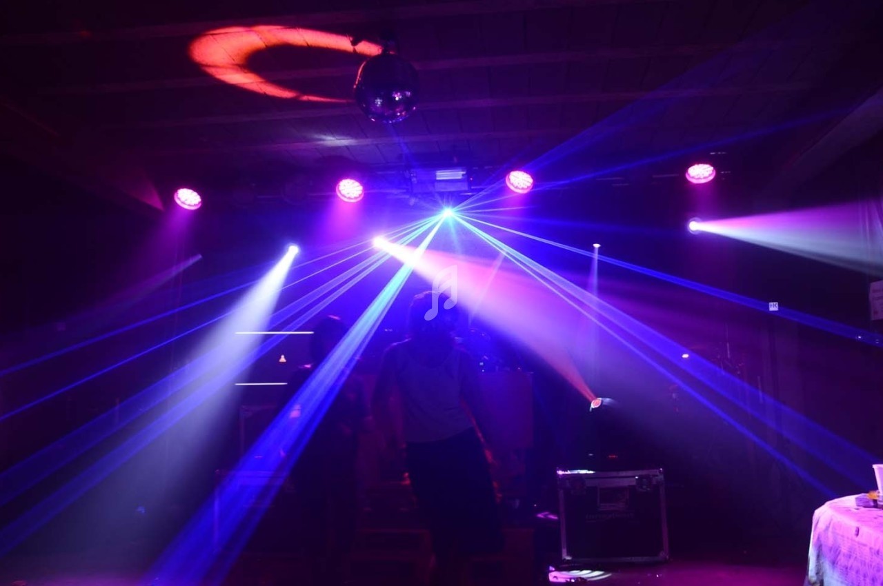 Jeune personne debout dans une salle sombre éclairée par des faisceaux lumineux colorés et une boule disco.