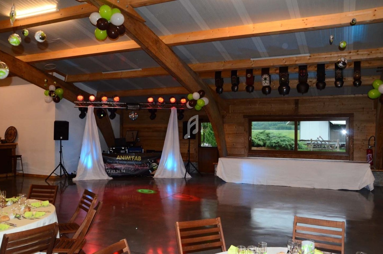 Salle de réception décorée avec des ballons, tables dressées et une piste de danse avec éclairage et matériel de DJ.