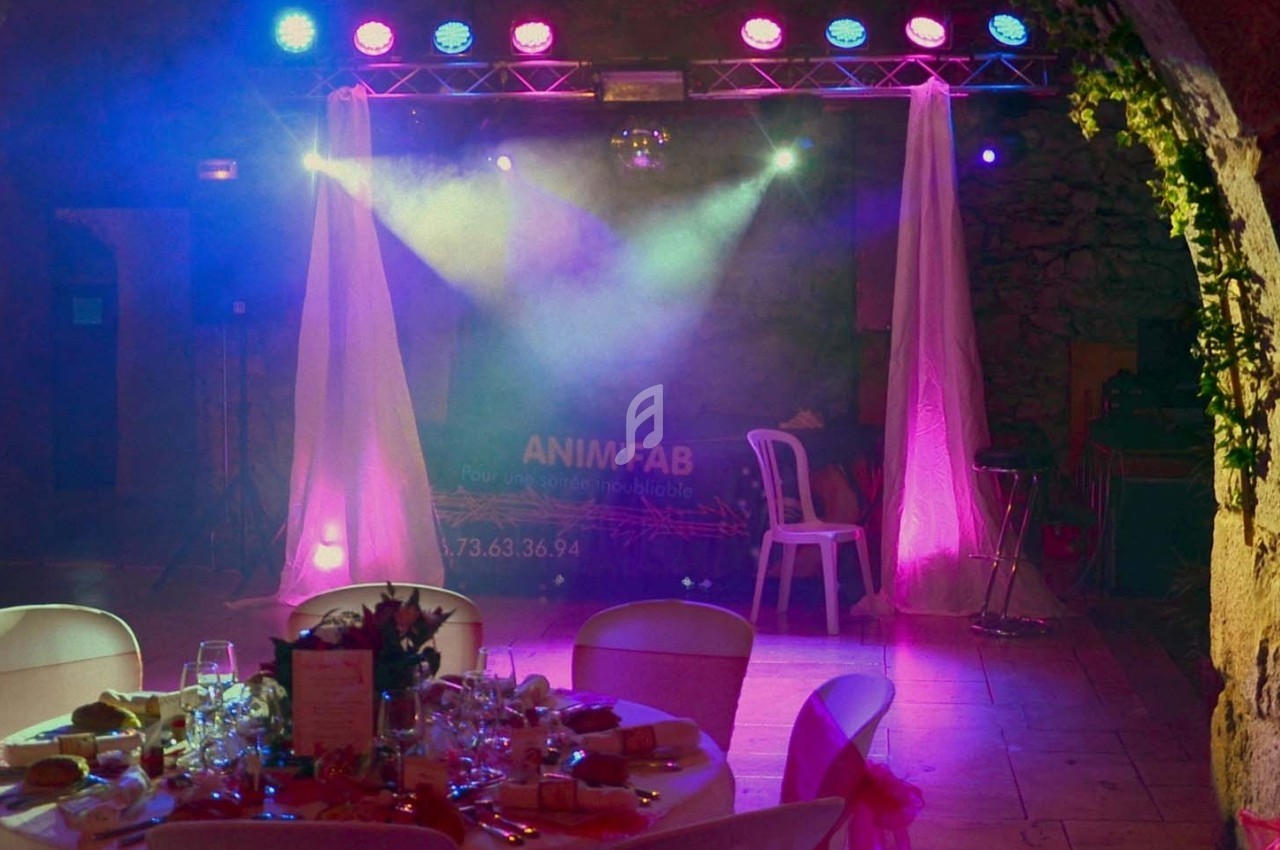 Scène éclairée avec des projecteurs colorés, rideaux blancs et tables dressées pour un événement festif en intérieur.