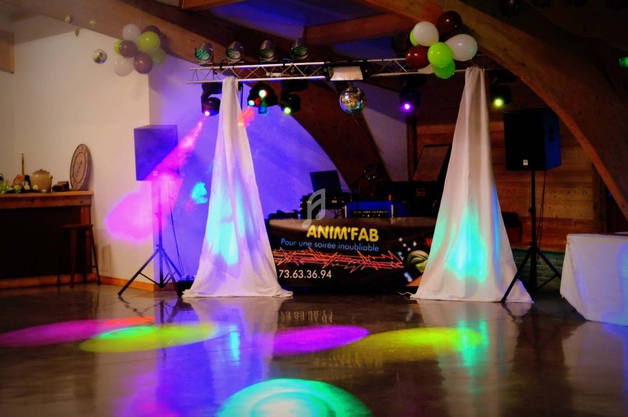 Salle de réception avec piste de danse éclairée par des lumières colorées et une table de DJ en arrière-plan.