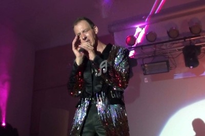 Miniature DJ Chignin (Savoie) - Anim'Fab #34 Un homme chante sur scène avec un micro, éclairé par une lumière rouge dans une ambiance sombre.