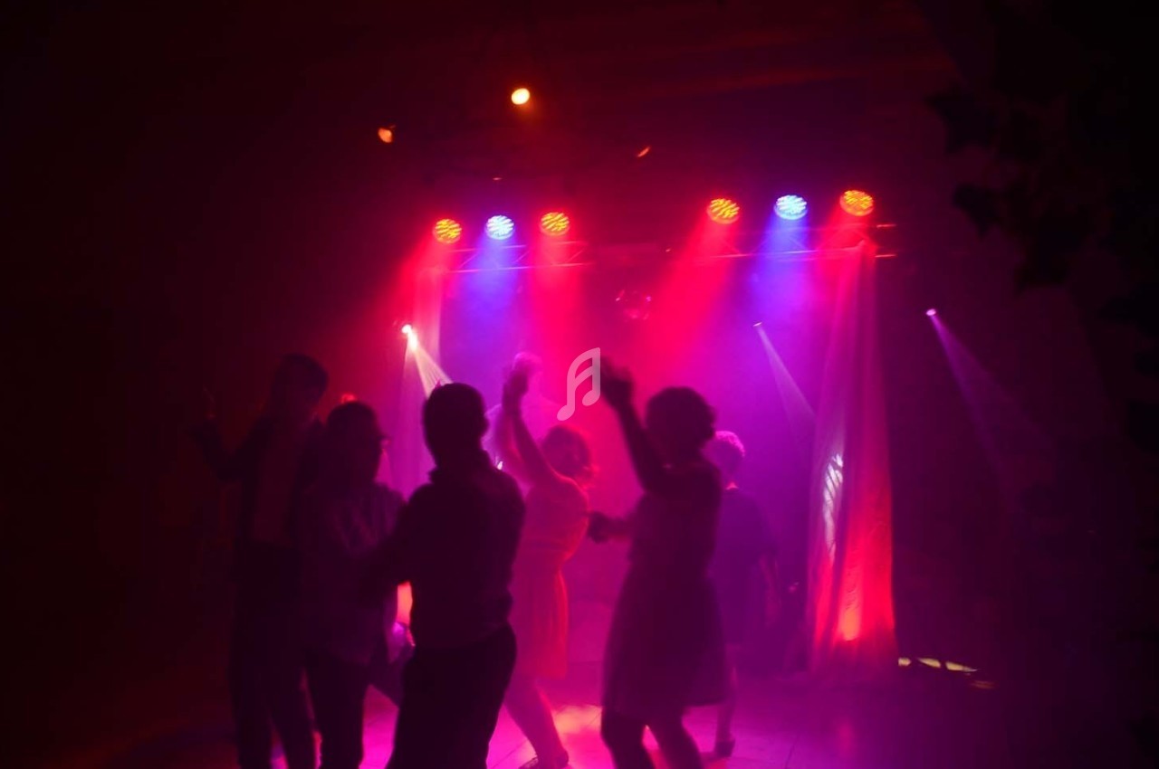 Personnes dansant sous des lumières colorées dans une ambiance tamisée et festive.