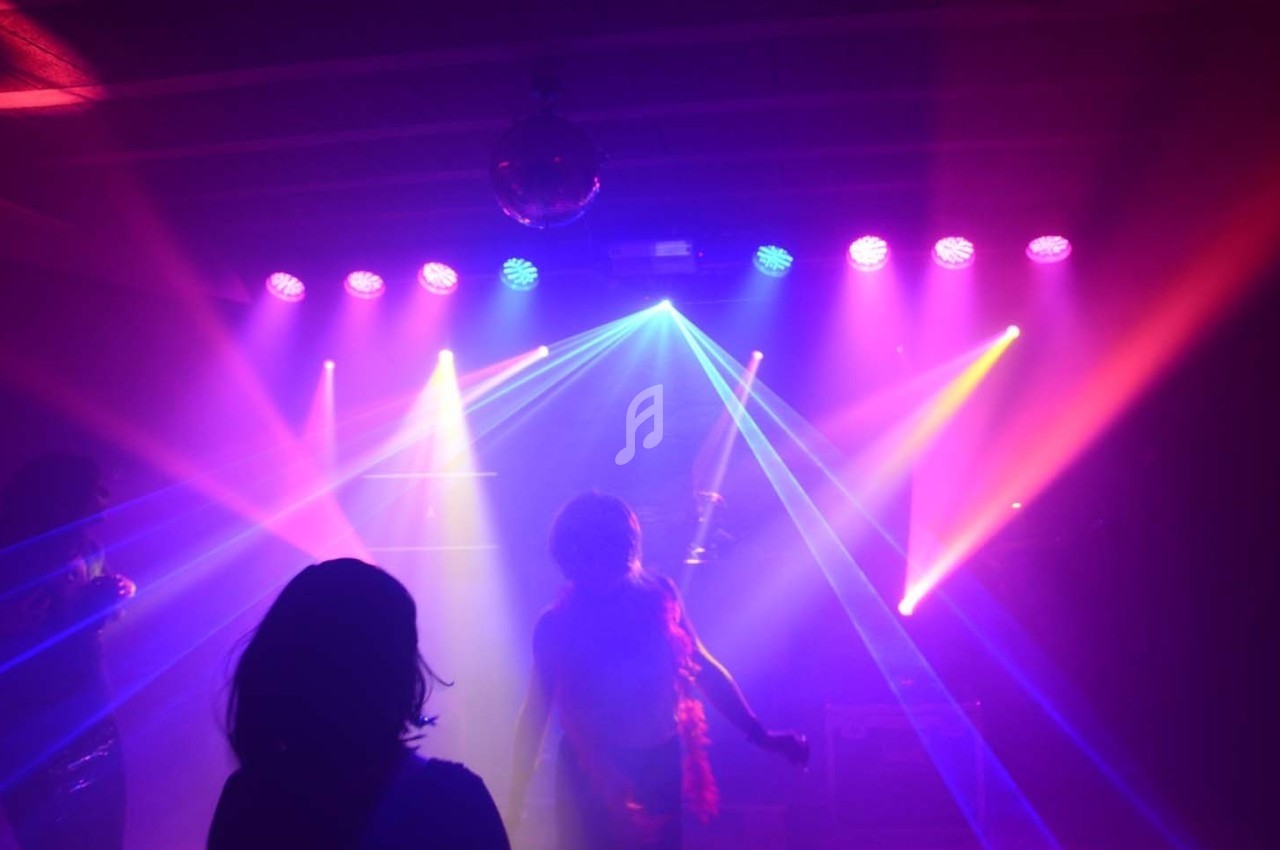 Personnes dans une salle sombre éclairée par des lumières colorées et des faisceaux laser.