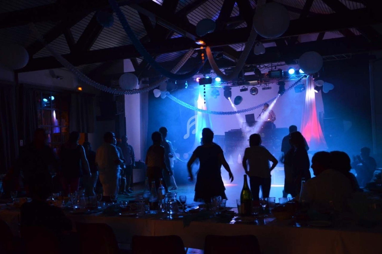 Personnes dansant dans une salle sombre décorée de guirlandes et éclairée par des lumières colorées.