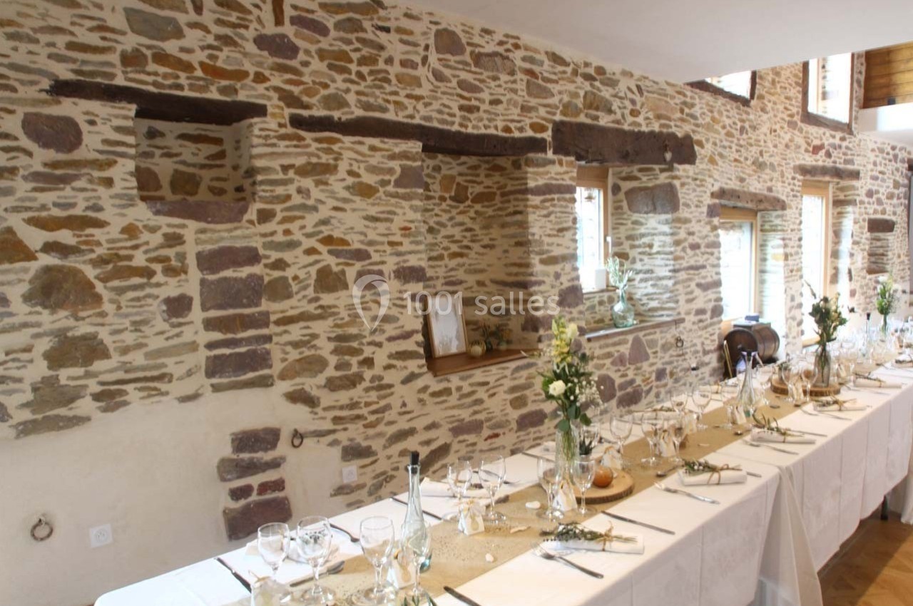 Salle en pierre avec tables décorées pour un repas, ornées de nappes blanches, fleurs et vaisselle élégante.