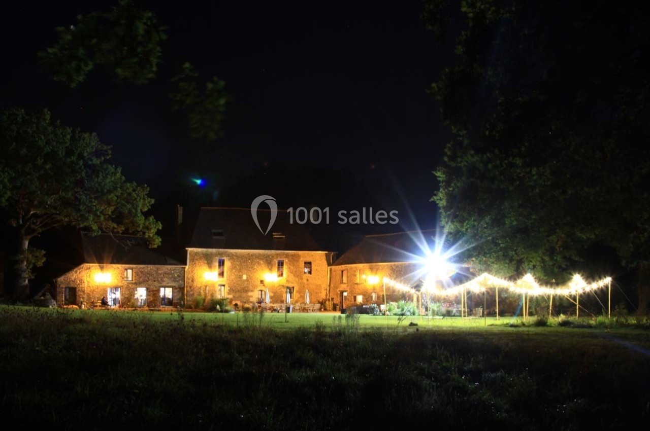 Bâtiment en pierre éclairé la nuit, entouré d'arbres et d'une guirlande lumineuse installée en extérieur.