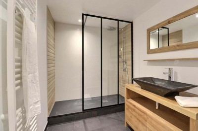 Douche à l'italienne avec paroi vitrée, carrelage beige et motifs, meuble en bois clair et miroir au mur.