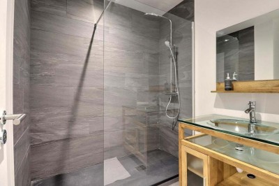 Douche à l'italienne avec paroi vitrée, carrelage beige et motifs, meuble en bois clair et miroir au mur.