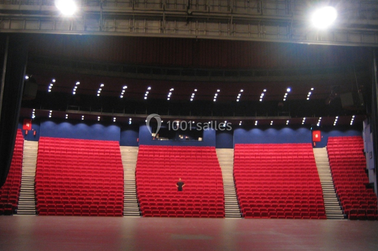 Salle de spectacle vide avec des rangées de sièges rouges, éclairée par des projecteurs au plafond.