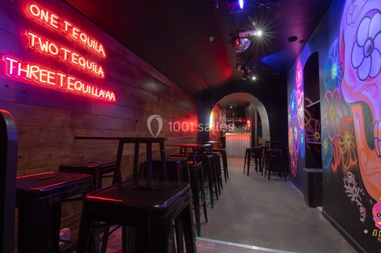 Bar avec murs décorés de graffitis colorés, éclairage néon et tabourets hauts alignés près de tables.