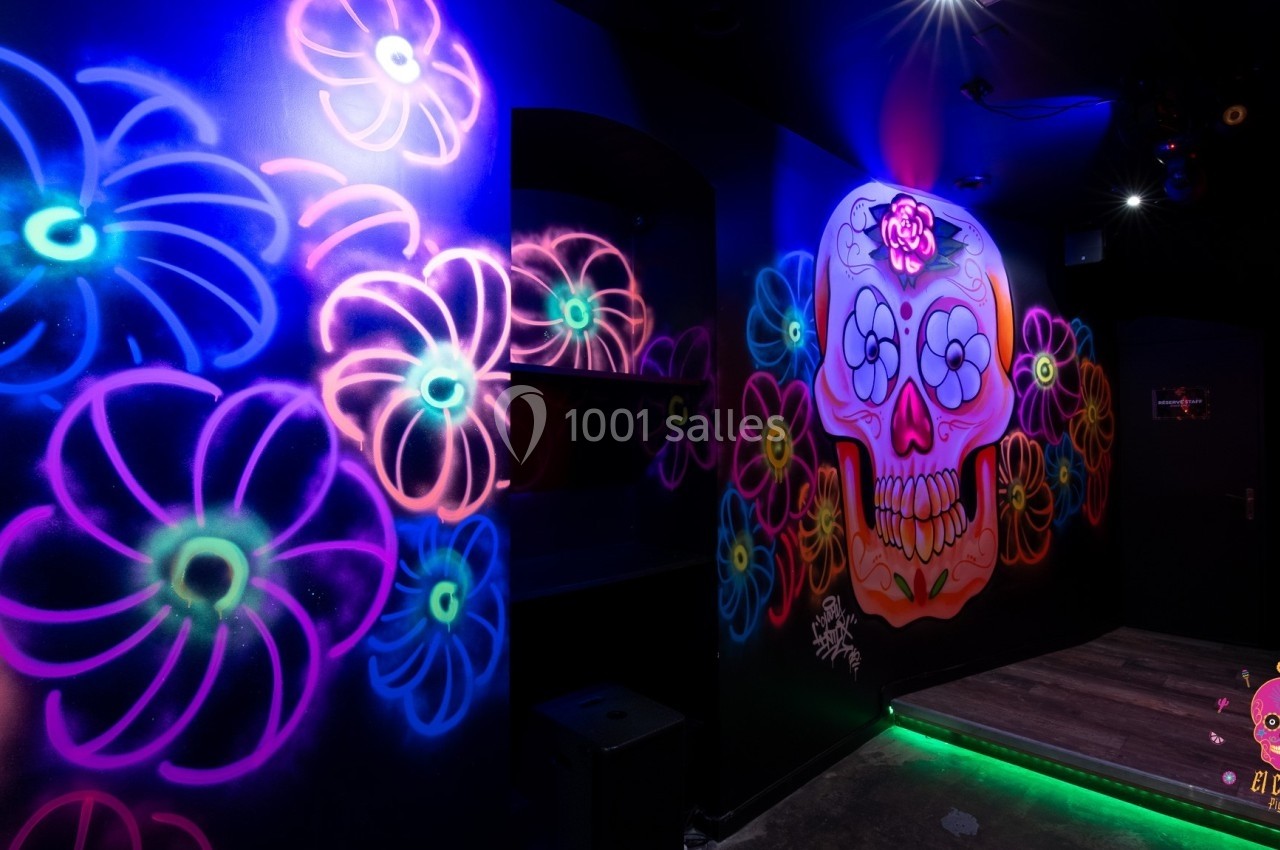Mur décoré de motifs fluorescents représentant des fleurs et un crâne coloré dans une ambiance sombre et lumineuse.
