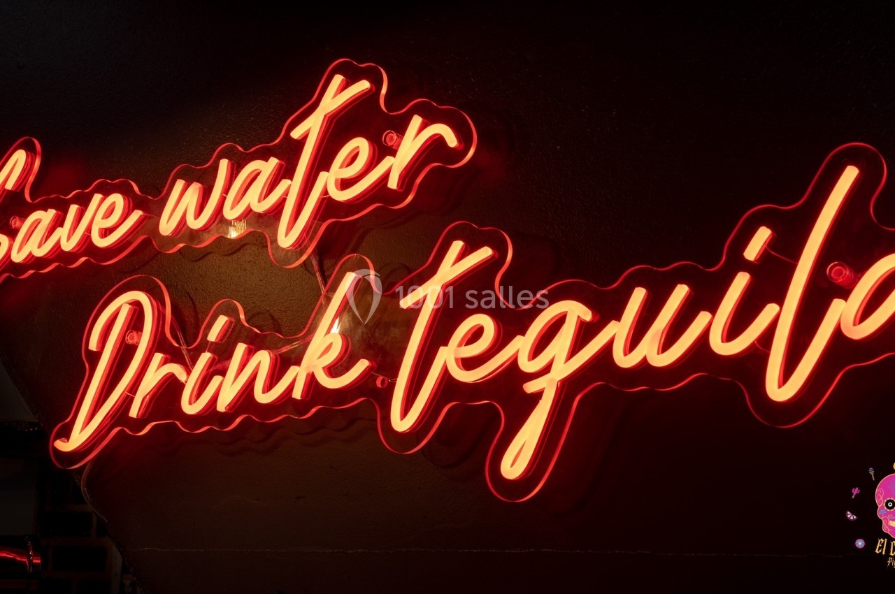 Enseigne néon rouge avec l'inscription ’Save water, Drink tequila’ sur un mur sombre.
