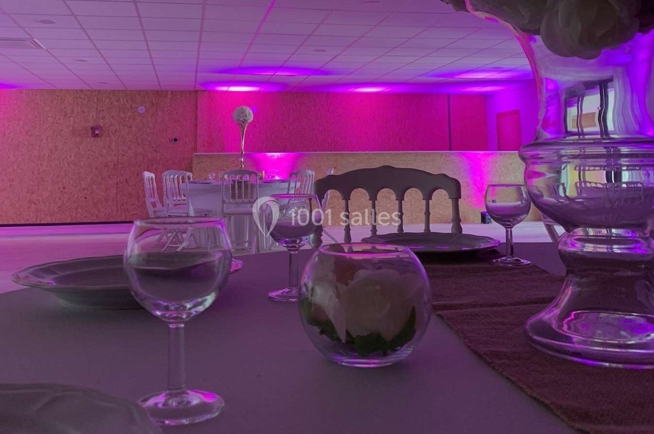 Salle de réception décorée avec des tables dressées, éclairage rose et chaises alignées en arrière-plan.