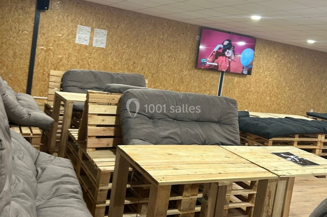 Des tables et canapés en palettes dans une salle avec un écran diffusant une personne tenant un ballon bleu.