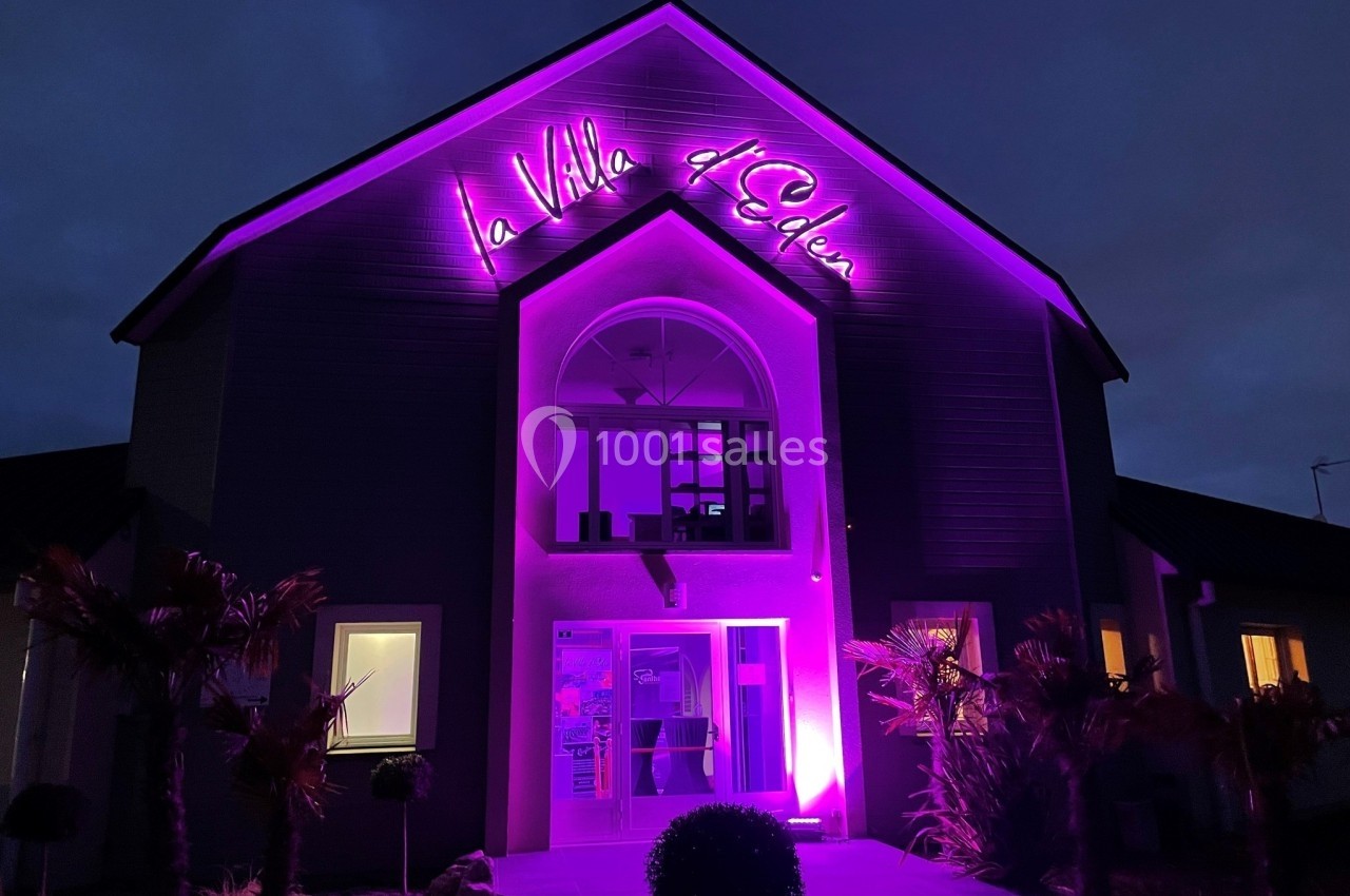 Façade d'un bâtiment éclairé en violet avec une enseigne lumineuse indiquant ’La Villa d'Eden’ de nuit.