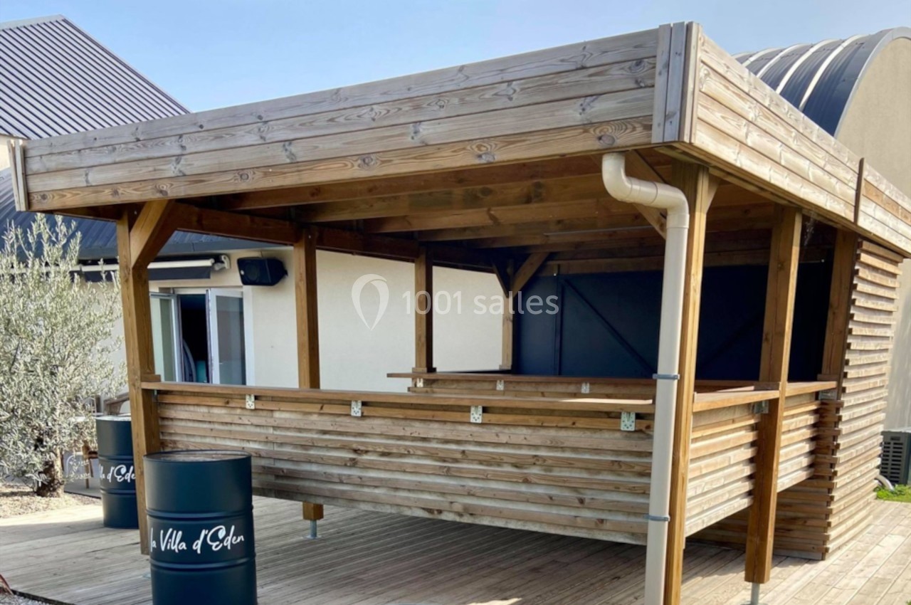 Kiosque en bois avec comptoir, situé sur une terrasse ensoleillée, entouré de barils décoratifs noirs.