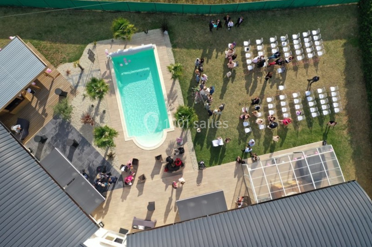 Vue aérienne d'une réception en extérieur avec piscine, chaises alignées pour une cérémonie et invités dispersés.