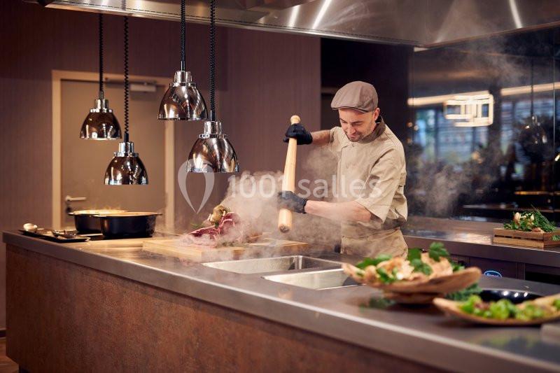 Un cuisinier prépare un plat chaud dans une cuisine professionnelle, utilisant un rouleau à pâtisserie.