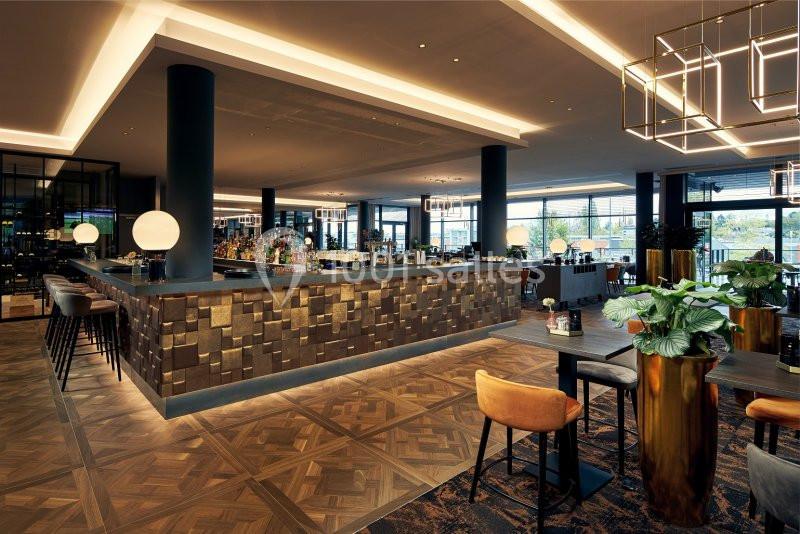 Bar moderne avec comptoir en bois texturé, éclairage chaleureux, tables et chaises élégantes dans un espace spacieux.