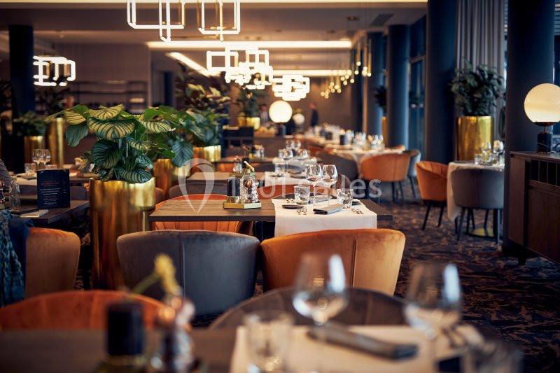 Location salle Nivelles (Brabant wallon) - Hôtel Nivelles Sud #4 Salle de restaurant élégante avec tables dressées, chaises colorées et plantes décoratives dans un éclairage chaleureux.