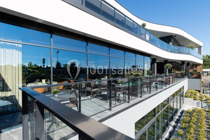 Location salle Nivelles (Brabant wallon) - Hôtel Nivelles Sud #7 Façade moderne d'un bâtiment avec de grandes baies vitrées et une terrasse aménagée avec des plantes et des sièges.