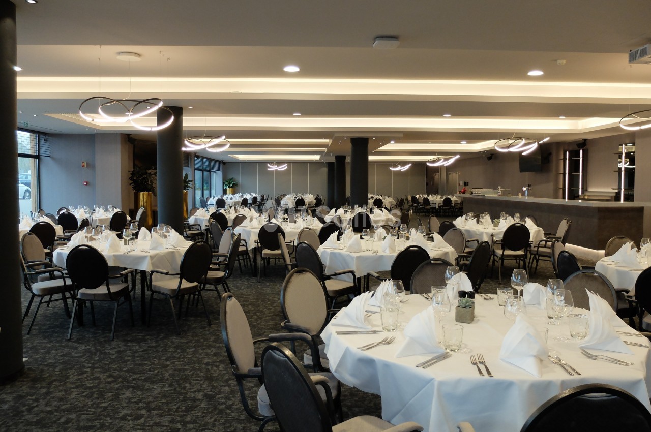 Salle de réception élégante avec tables rondes dressées de nappes blanches, verres et serviettes pliées.