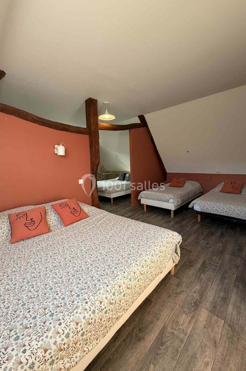 Chambre spacieuse avec un lit double, deux lits simples, parquet au sol et murs partiellement peints en terracotta.