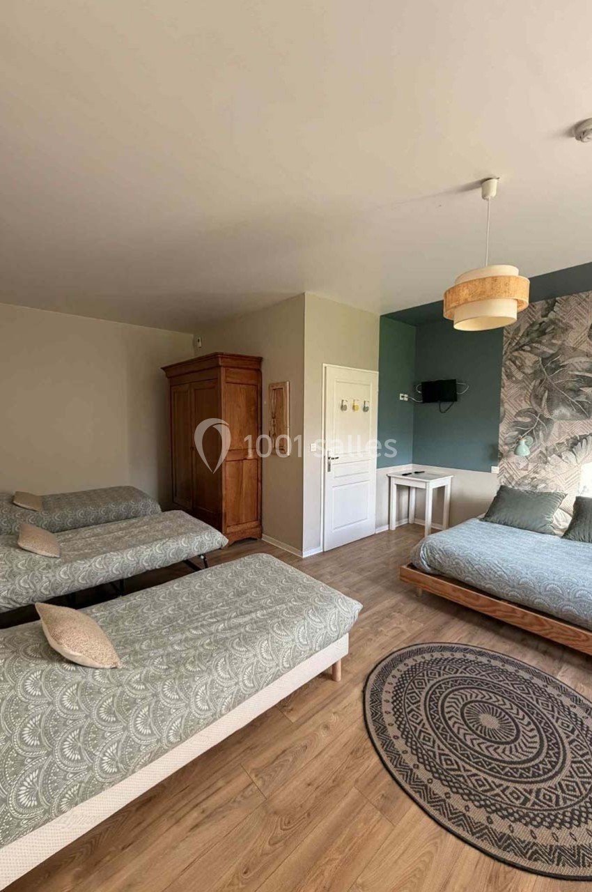 Chambre lumineuse avec trois lits simples, un lit double, une armoire en bois, un bureau et un tapis rond sur parquet.