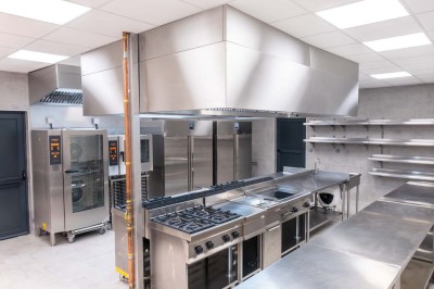 Miniature Location salle Saint-Laurent-Blangy (Pas-de-Calais) - Elegance Events #18 Cuisine professionnelle moderne avec équipements en inox, éclairage suspendu et fourneaux sous une hotte d'extraction.