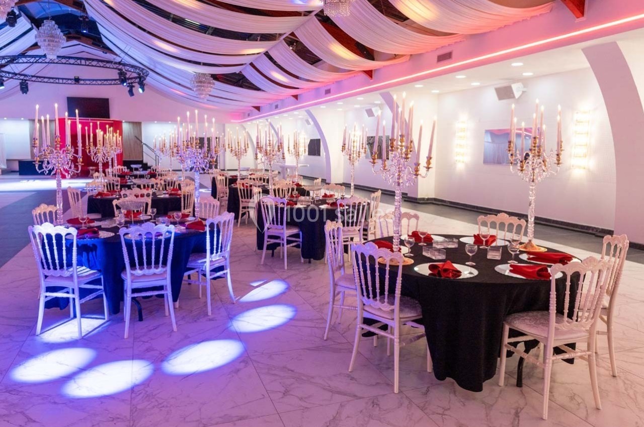 Salle de réception élégante avec tables rondes dressées, nappes noires, chandeliers et éclairage tamisé.