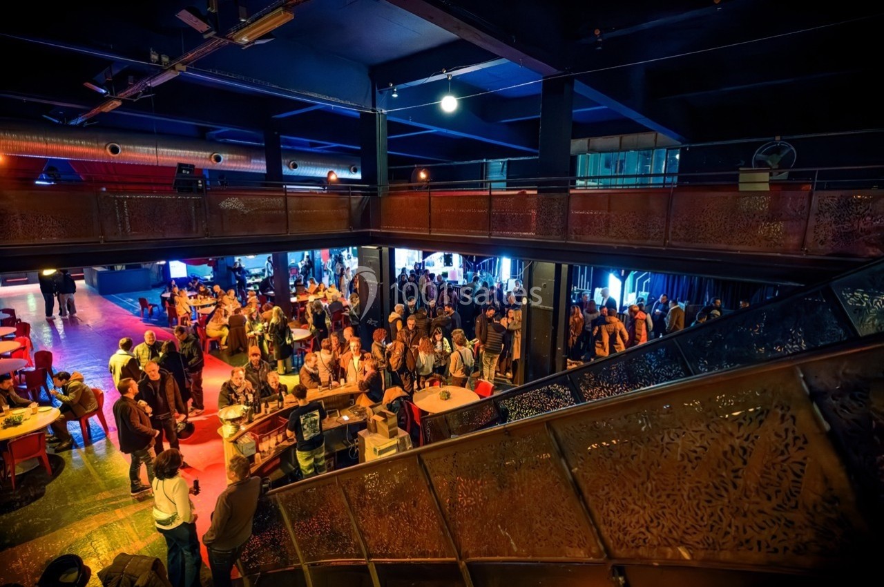 Vue intérieure d'un espace culturel animé avec des groupes de personnes discutant et se rassemblant autour de tables.