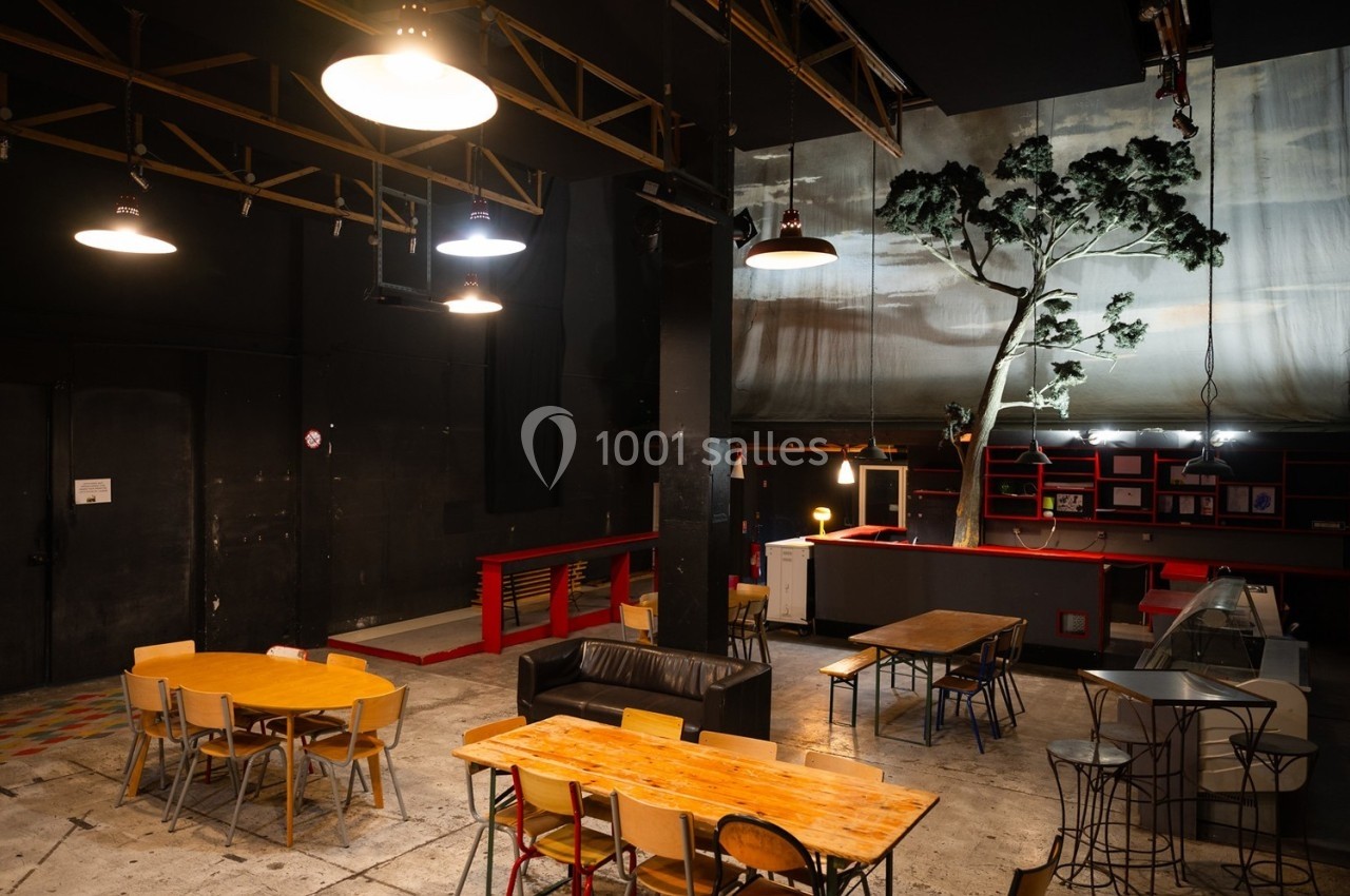 Salle intérieure avec tables, chaises, canapé et décor de scène comprenant un arbre artificiel et un éclairage tamisé.