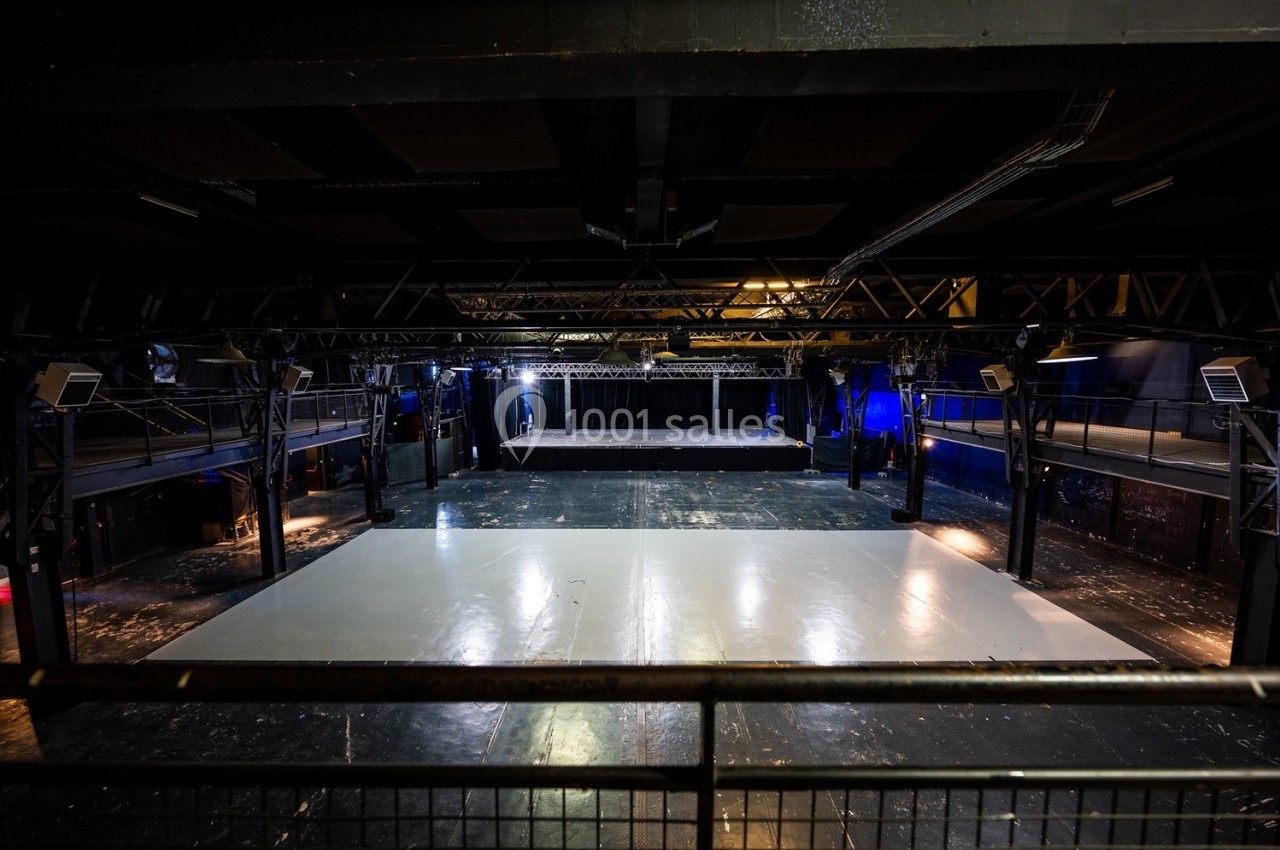 Salle de spectacle vide avec scène au fond, éclairage tamisé et structure métallique apparente.