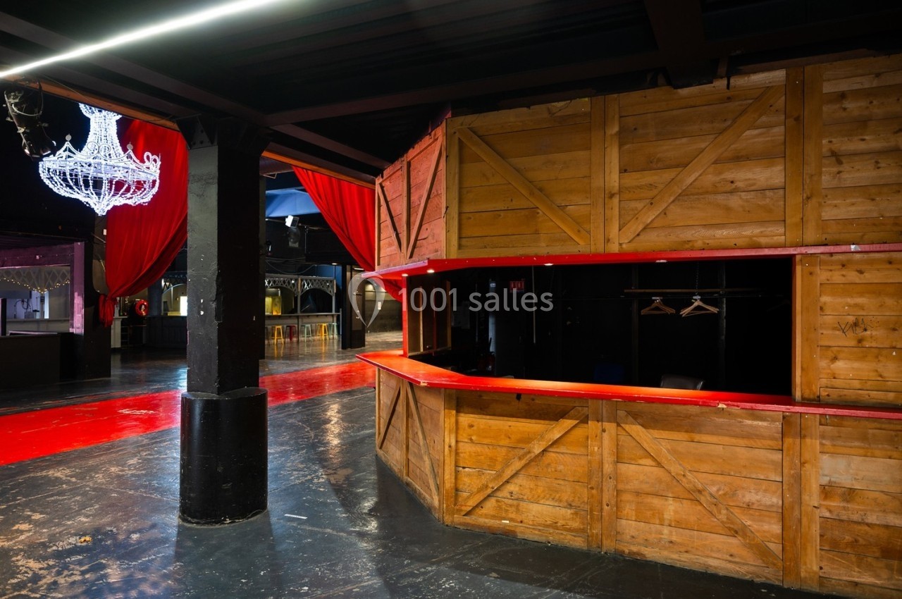 Intérieur d'une salle avec un comptoir en bois, des rideaux rouges et un lustre suspendu.