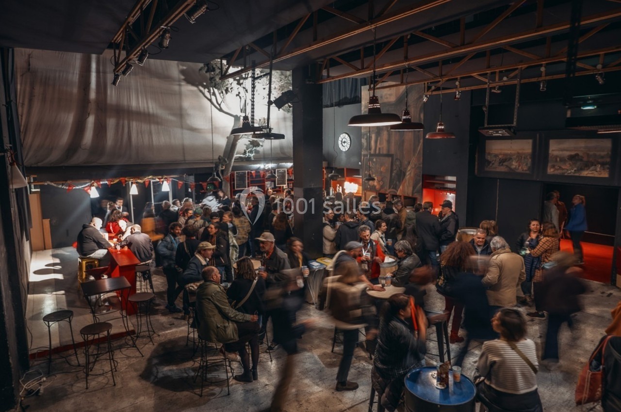 Groupe de personnes rassemblées dans un espace intérieur animé avec des tables, un bar et une lumière tamisée.
