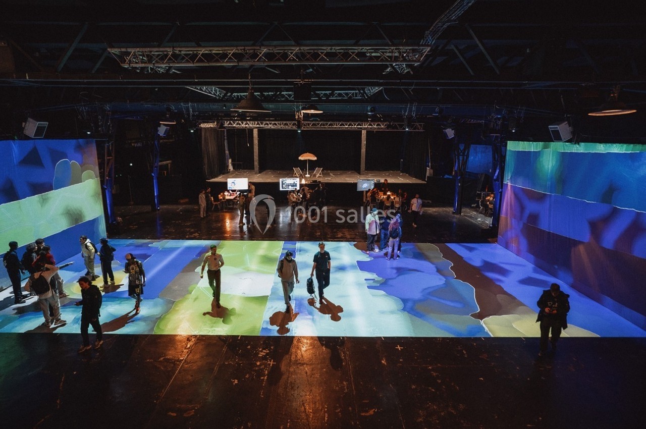 Des visiteurs marchent dans une salle sombre avec des projections lumineuses colorées au sol et sur les murs.
