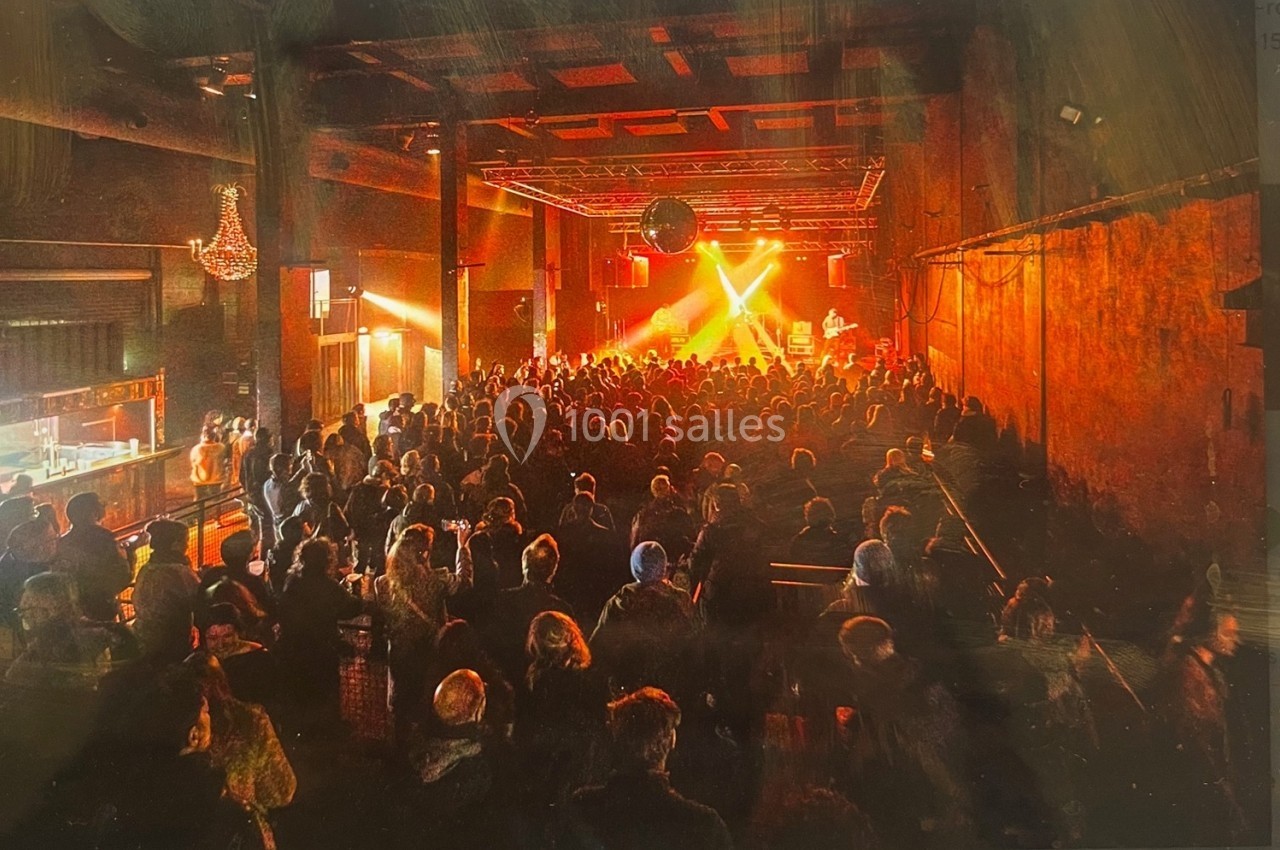 Salle de concert sombre avec une foule debout face à une scène éclairée par des projecteurs rouges et jaunes.